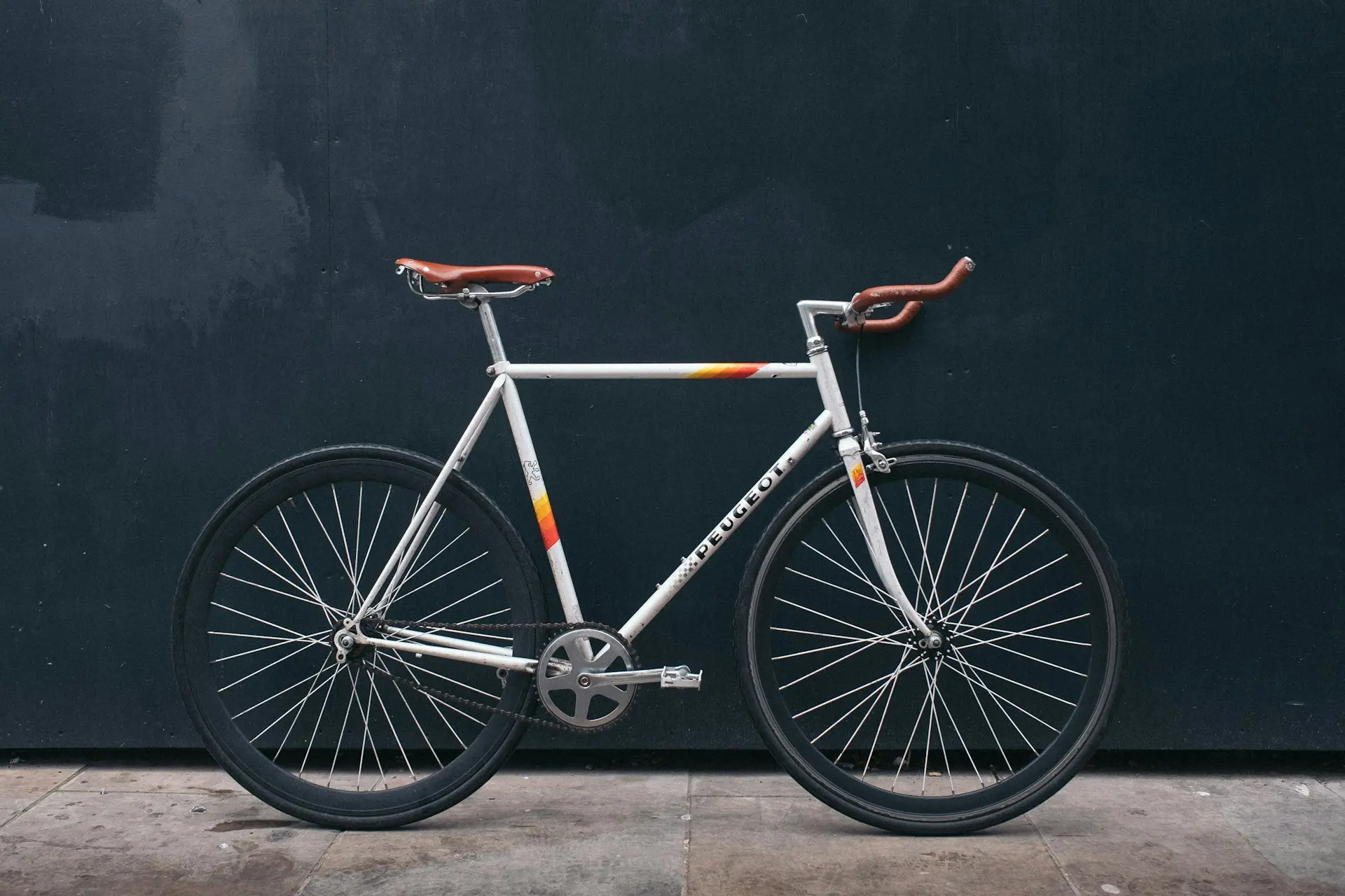 bicicleta fixie gris apoyada en una pared negra